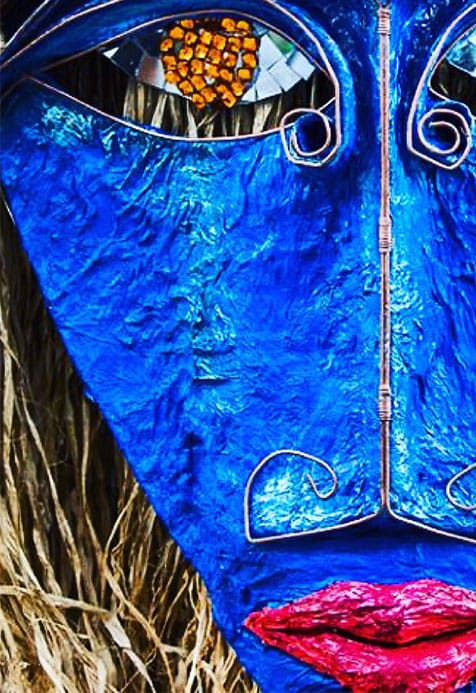 Close-up of an abstract blue face sculpture with metallic details, textured surface, red lips, and a mosaic pattern in one eye.