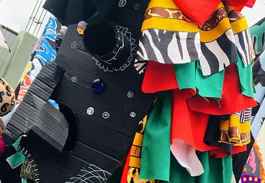 A close-up of a colourful costume featuring black card with drawn gears and fabric strips in red, green, yellow, zebra, and leopard patterns.