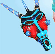 A colourful mask with blue, red, and black patterns and two long, blue horns against a light blue background.